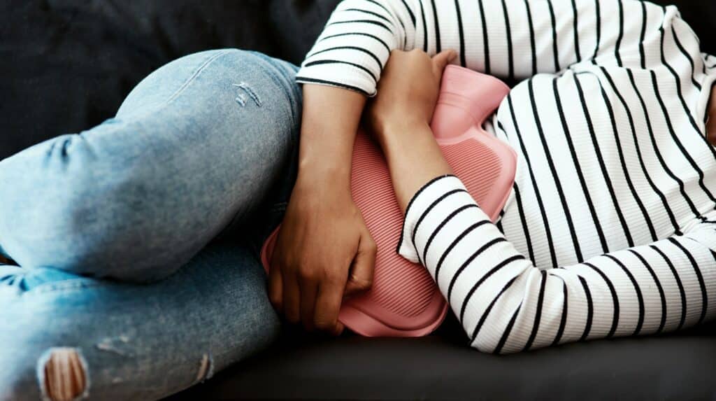 Cropped shot of a woman holding a hot water bottle against her stomach on the sofa at home