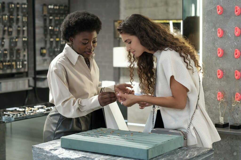 Young woman looking at ring held by African shop assistant