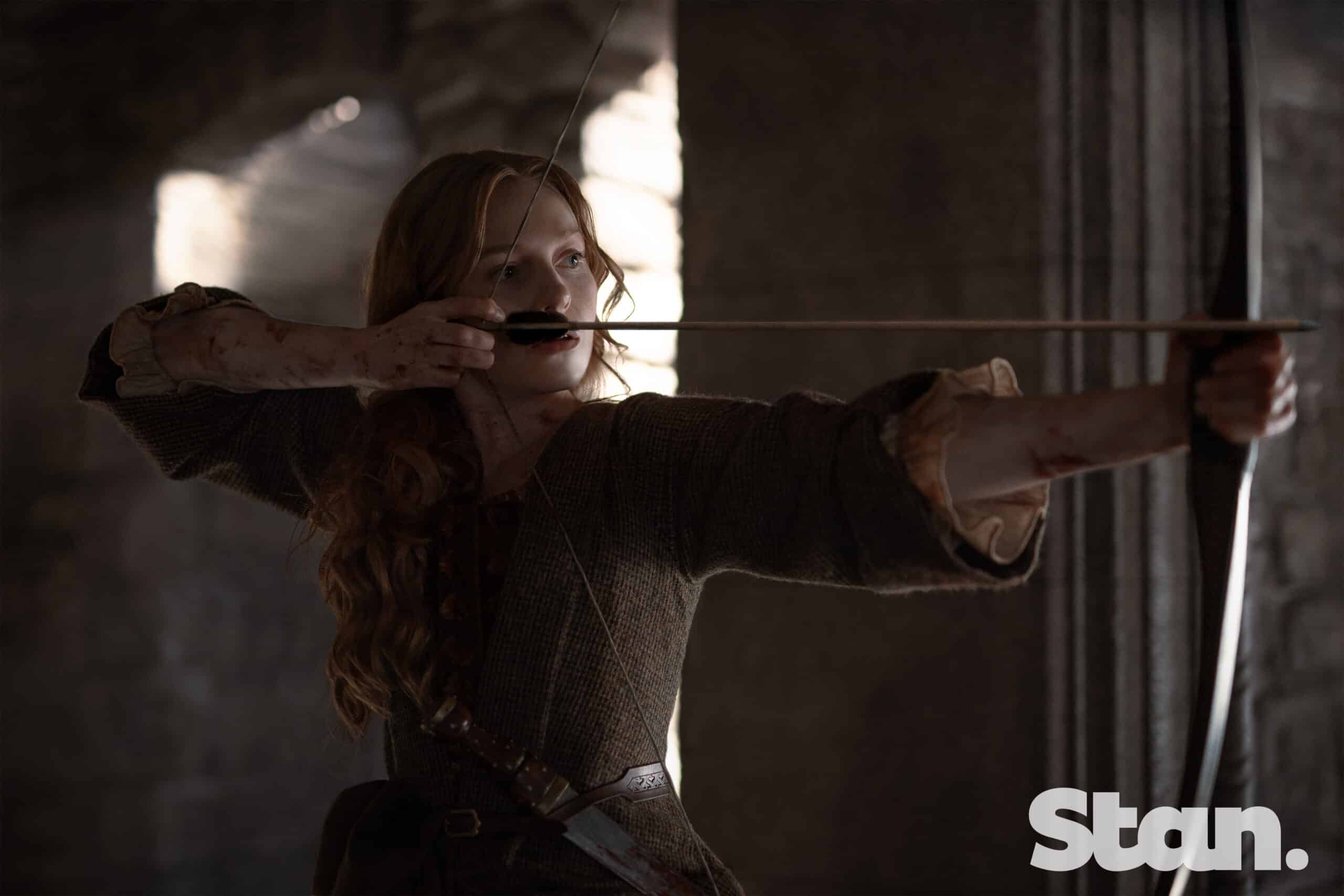 Ellen MacKenzie aims a bow inside a stone hall