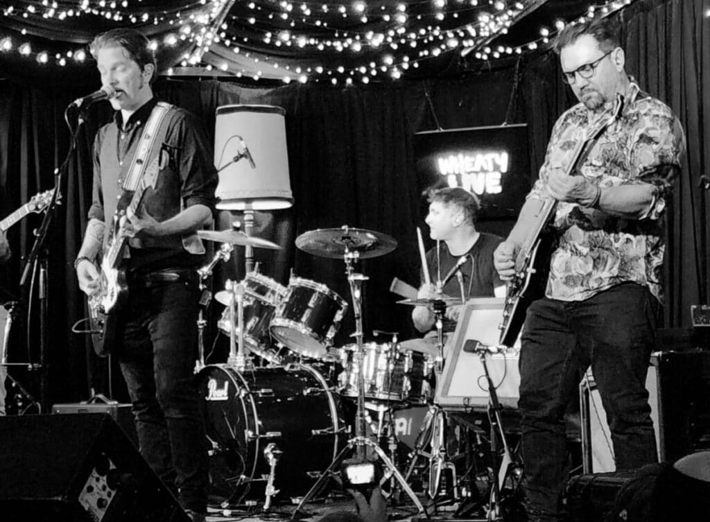 Fuselage performing beneath strings of lights at the Wheaty in a black and white photograph
