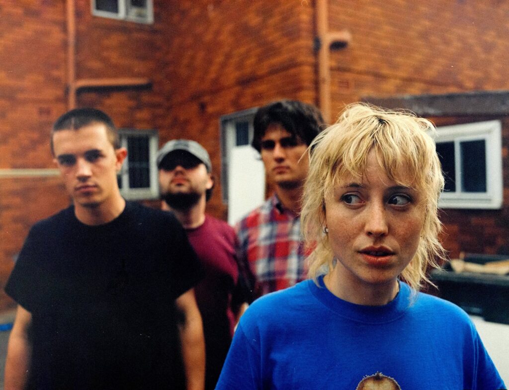 Swapmeet gathered outside a brick building in an Olive Rush publicity photograph