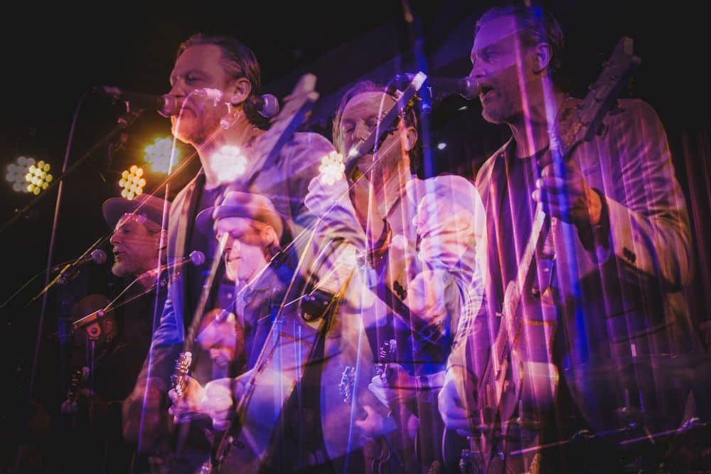 Layered live-performance photograph of Sean Power and The Main Street Band in purple stage lighting