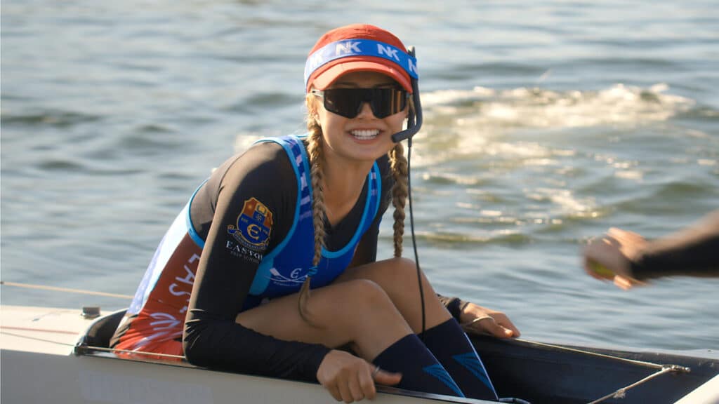 Teagan smiles from the coxswain seat of a rowing shell in Crew Girl