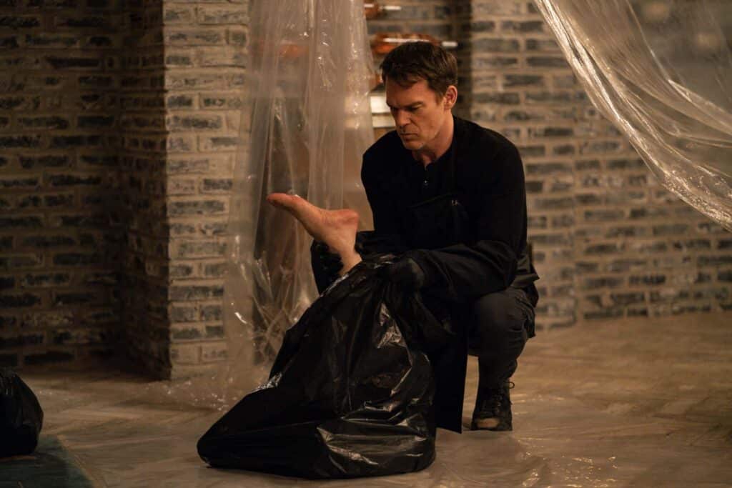 Dexter Morgan kneeling beside a black bag in a plastic-lined room in Dexter Resurrection season two