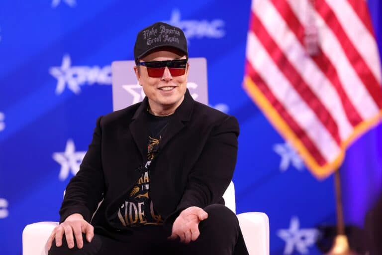 Elon Musk wearing a cap and sunglasses while speaking at CPAC in February 2025.