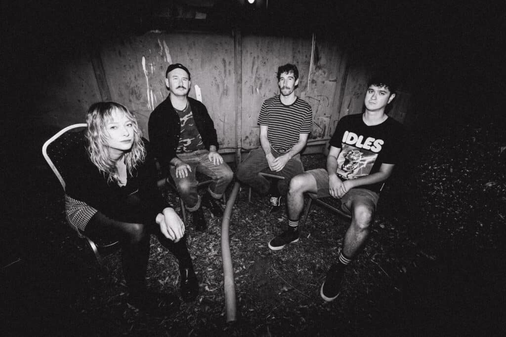Dvrkworld seated outdoors beside a timber fence in a black-and-white portrait