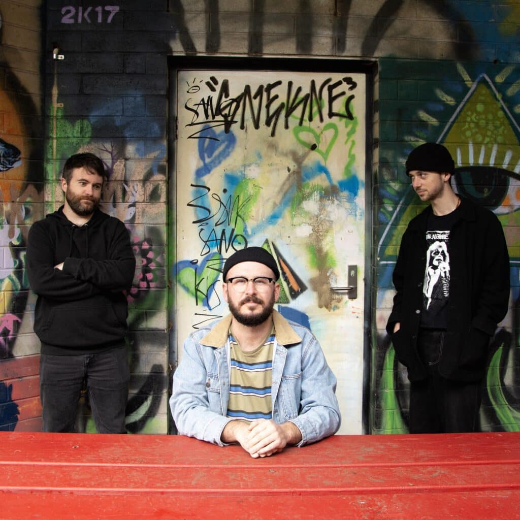 TEENS in casual dark clothes and a denim jacket beside a red table and graffiti-covered wall