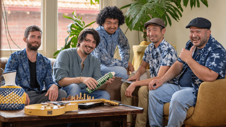 The five musicians of G_Tano smiling around a table with a guitar and chessboard