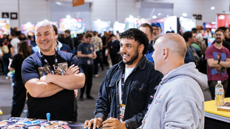 Three PAX Australia attendees chatting beside an arcade controller on the busy show floor