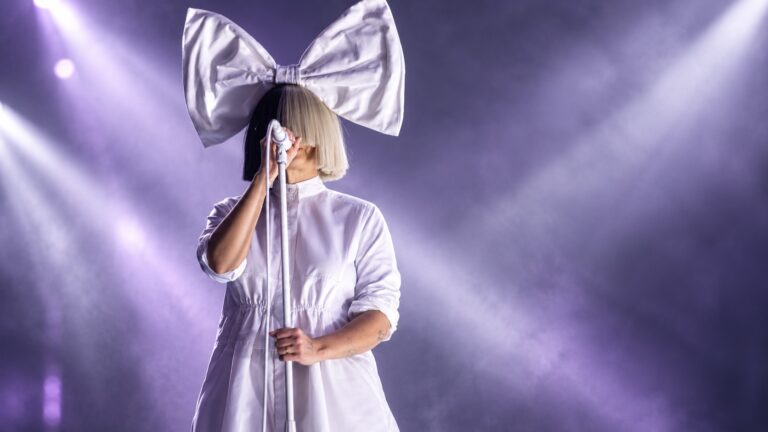 Sia performing onstage beneath a silver bow and purple lighting