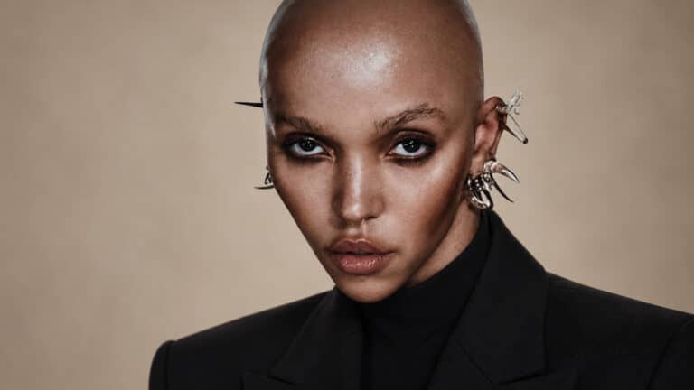 FKA twigs in a black high-neck blazer against a warm studio background