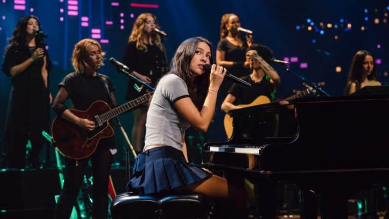 Olivia Rodrigo sings at a piano with her band and backing vocalists on the Austin City Limits stage.