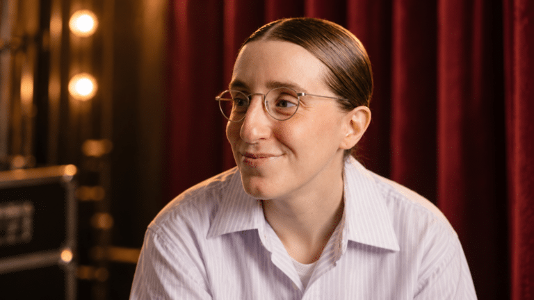 Robby Hoffman smiles backstage in front of a burgundy theatre curtain