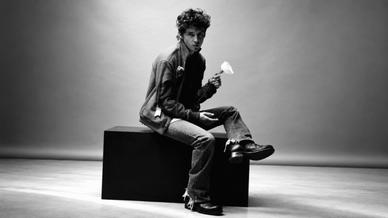 Troye Sivan holding a white rose in a black-and-white studio portrait