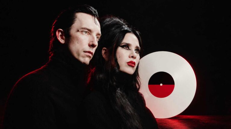 Twin Temple posed beside a white vinyl record in a dark red room