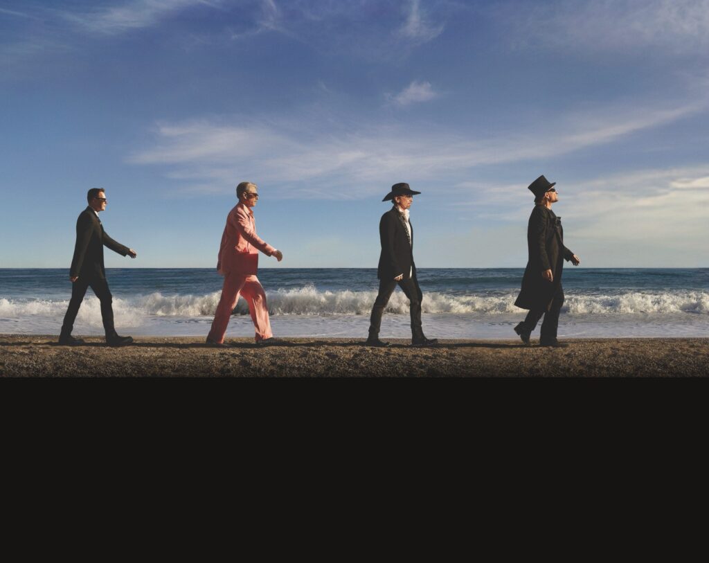 The four members of U2 walking along a beach