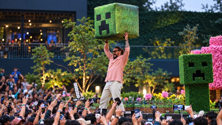 Jason Momoa raises a Minecraft Creeper block above a crowd at a live event